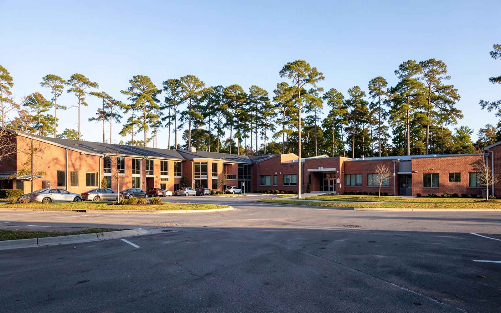 A brick suburban school campus framed by tall pines on a clear Carolina morning